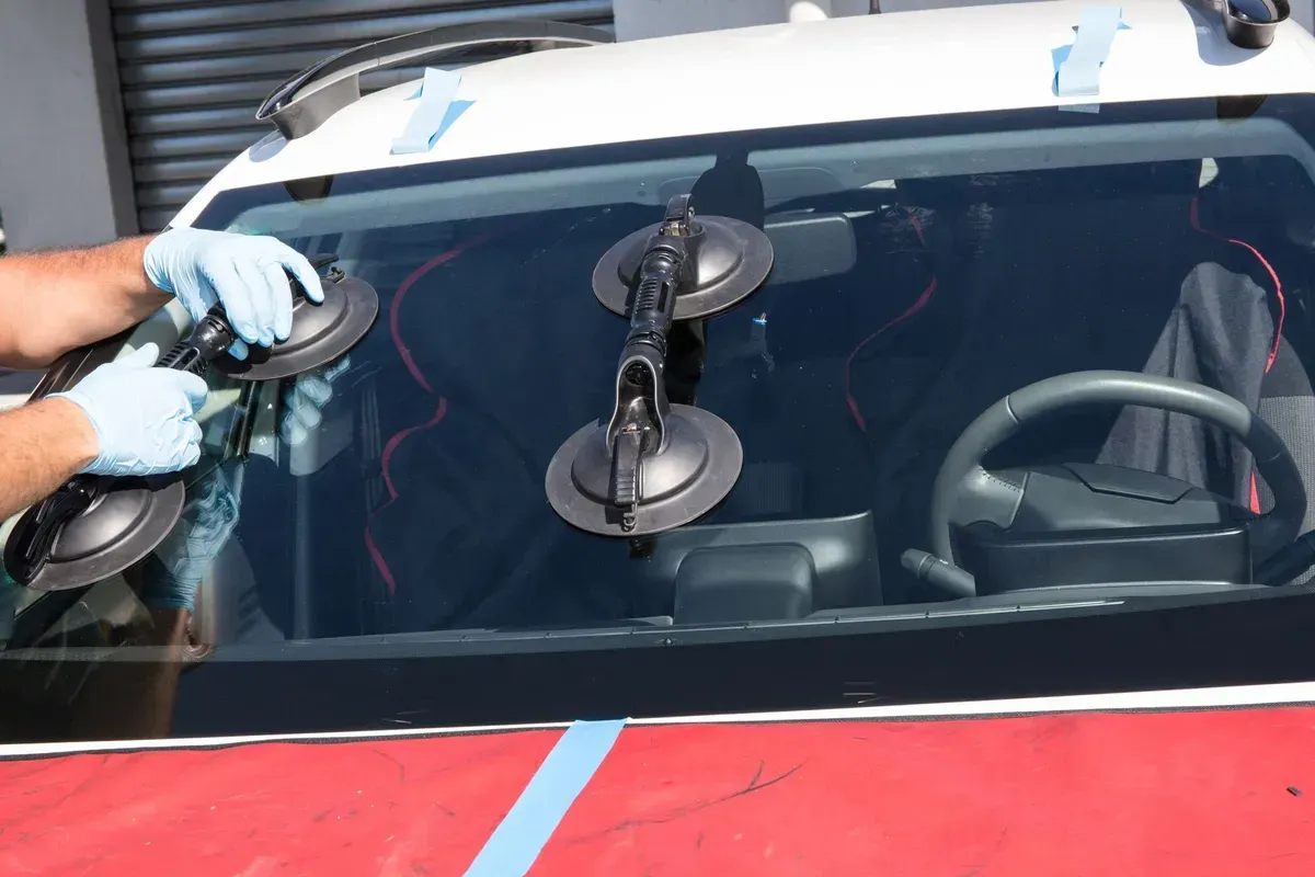 Person using suction cups to lift a windshield from a red and white car.