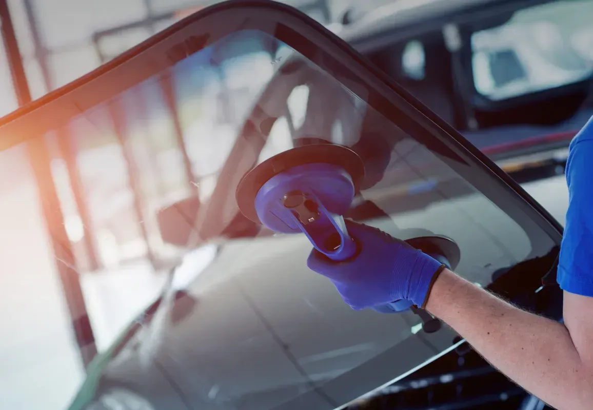 Person with blue gloves uses a suction cup tool on a car windshield.