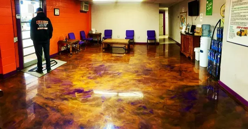 A person in a black jacket stands by a door in a waiting room with a reflective, colorful epoxy floor.
