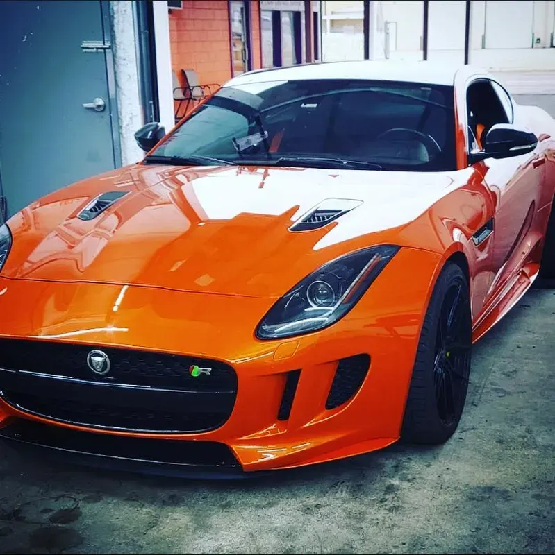 Orange and white Jaguar F-Type sports car parked in front of a building with a black front spoiler and black wheels.