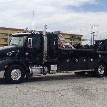 A black tow truck is parked in a parking lot