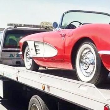 A red convertible is being towed by a tow truck.