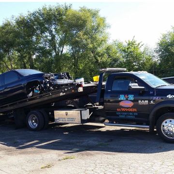 A black car is being towed by a tow truck.