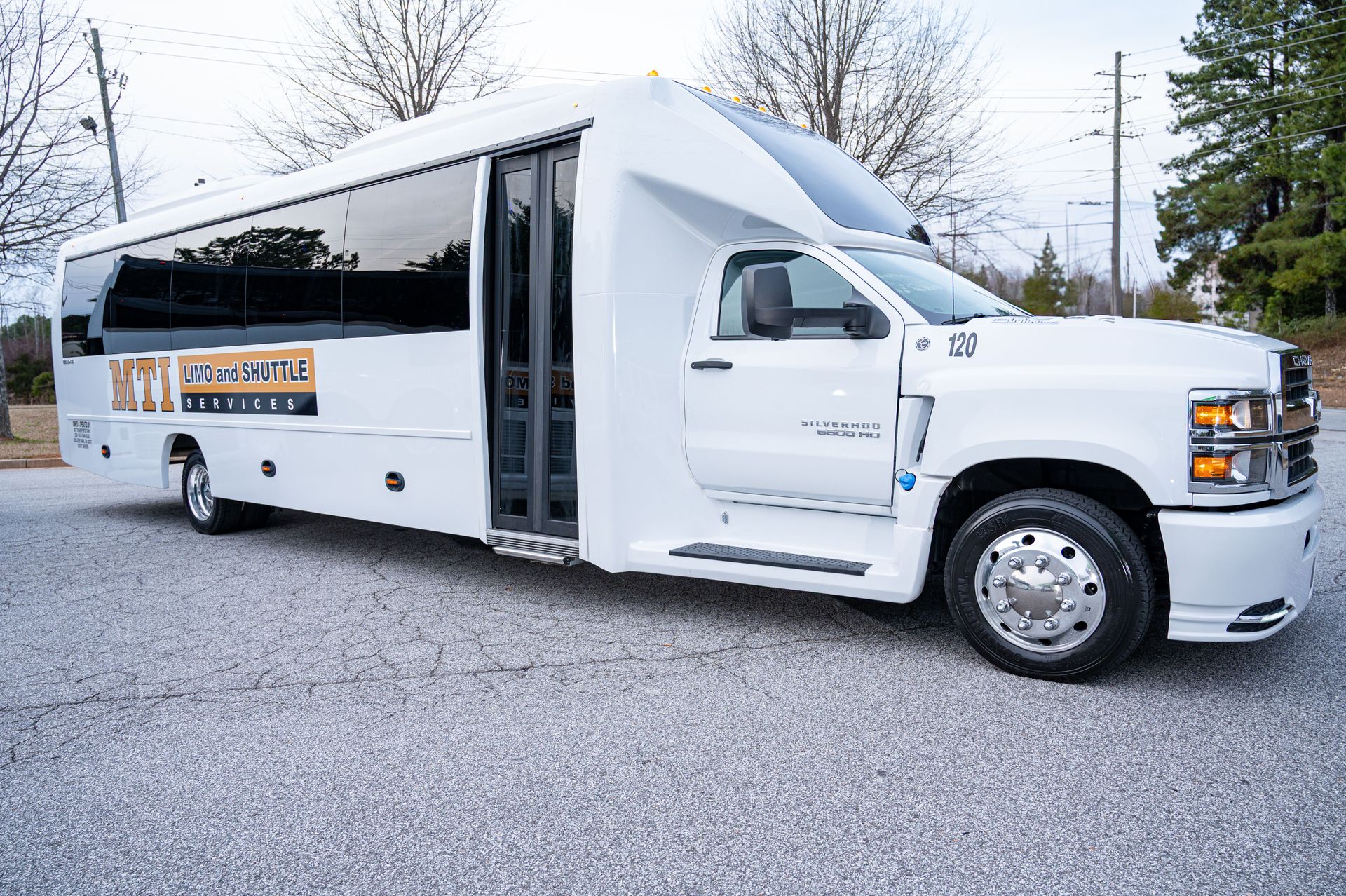 White shuttle bus with open side door parked on gravel lot with trees in the background