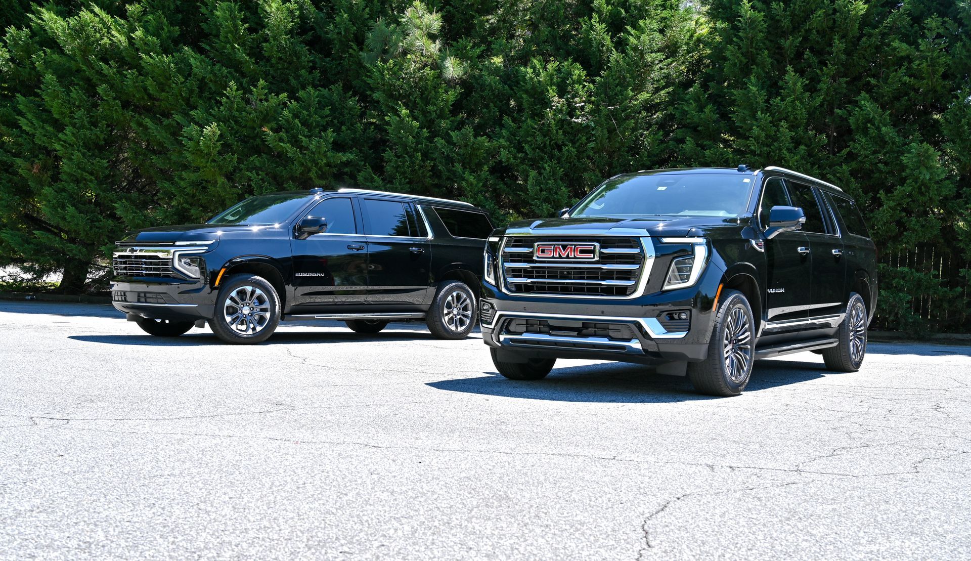 Two black SUVs parked on a sunny road with trees in the background