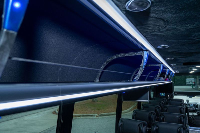 Blue-lit bus interior with rows of seats and overhead handrails