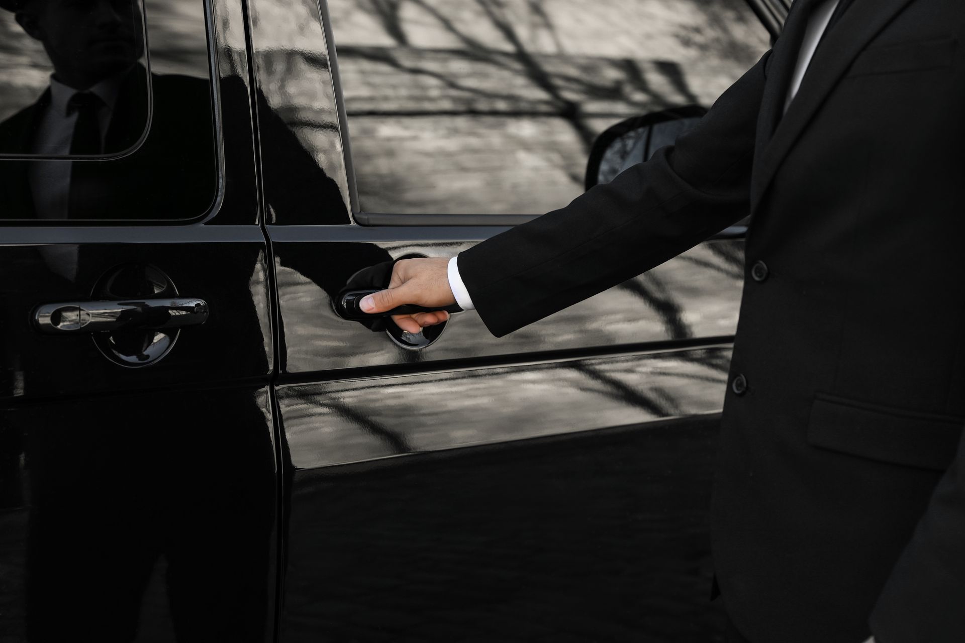 A person in a black suit opens a black car door with a keyless handle.