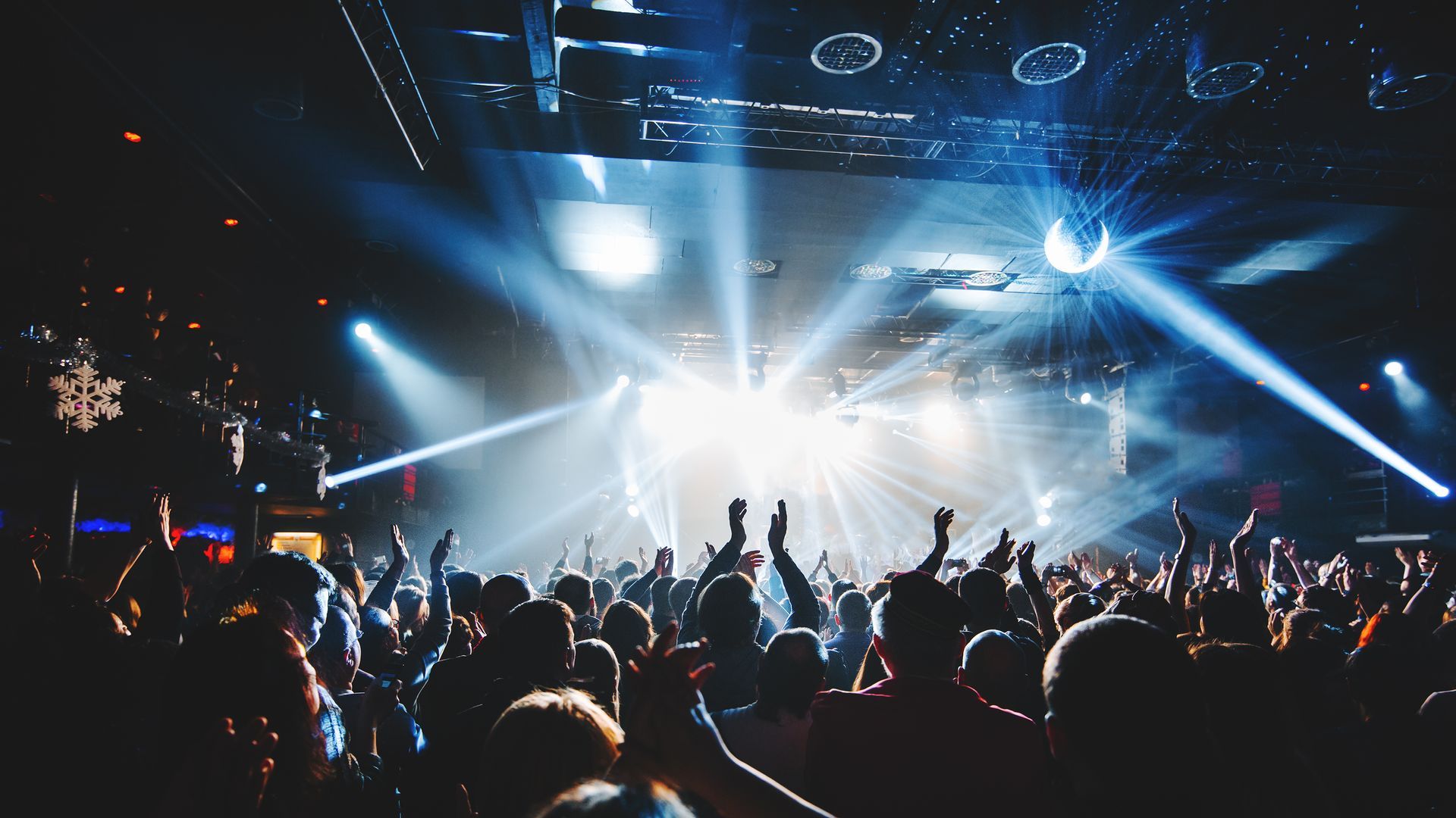 Crowd at a concert with bright white stage lights and raised hands in a dark venue