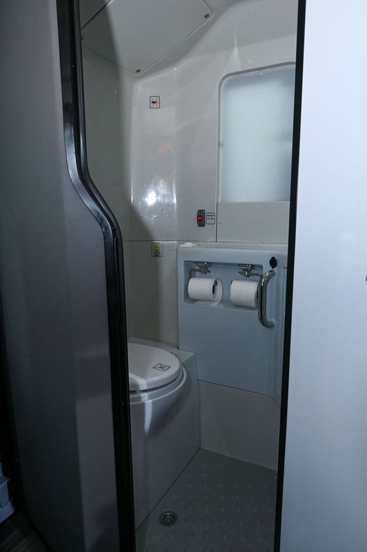 Compact restroom on a train or plane with a toilet, sink, and toilet paper dispenser.