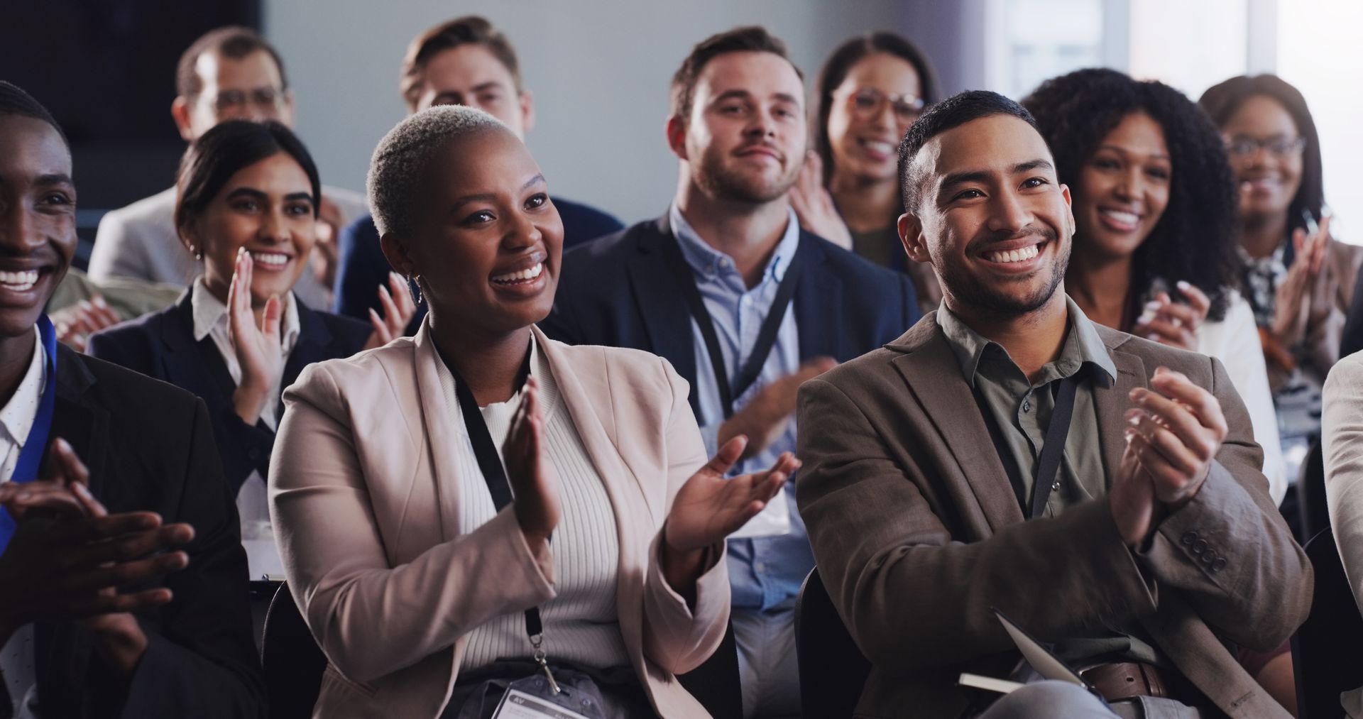 Audience in business attire clapping and smiling at a presentation.