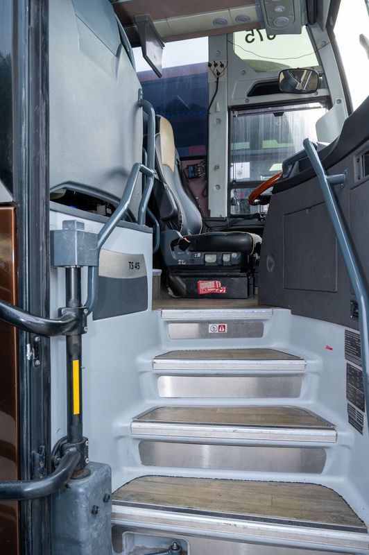 Bus entrance with metal steps and handrails leading to the driver’s area.
