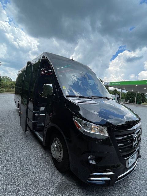 Black luxury van parked on wet pavement under a cloudy sky, front three-quarter view.