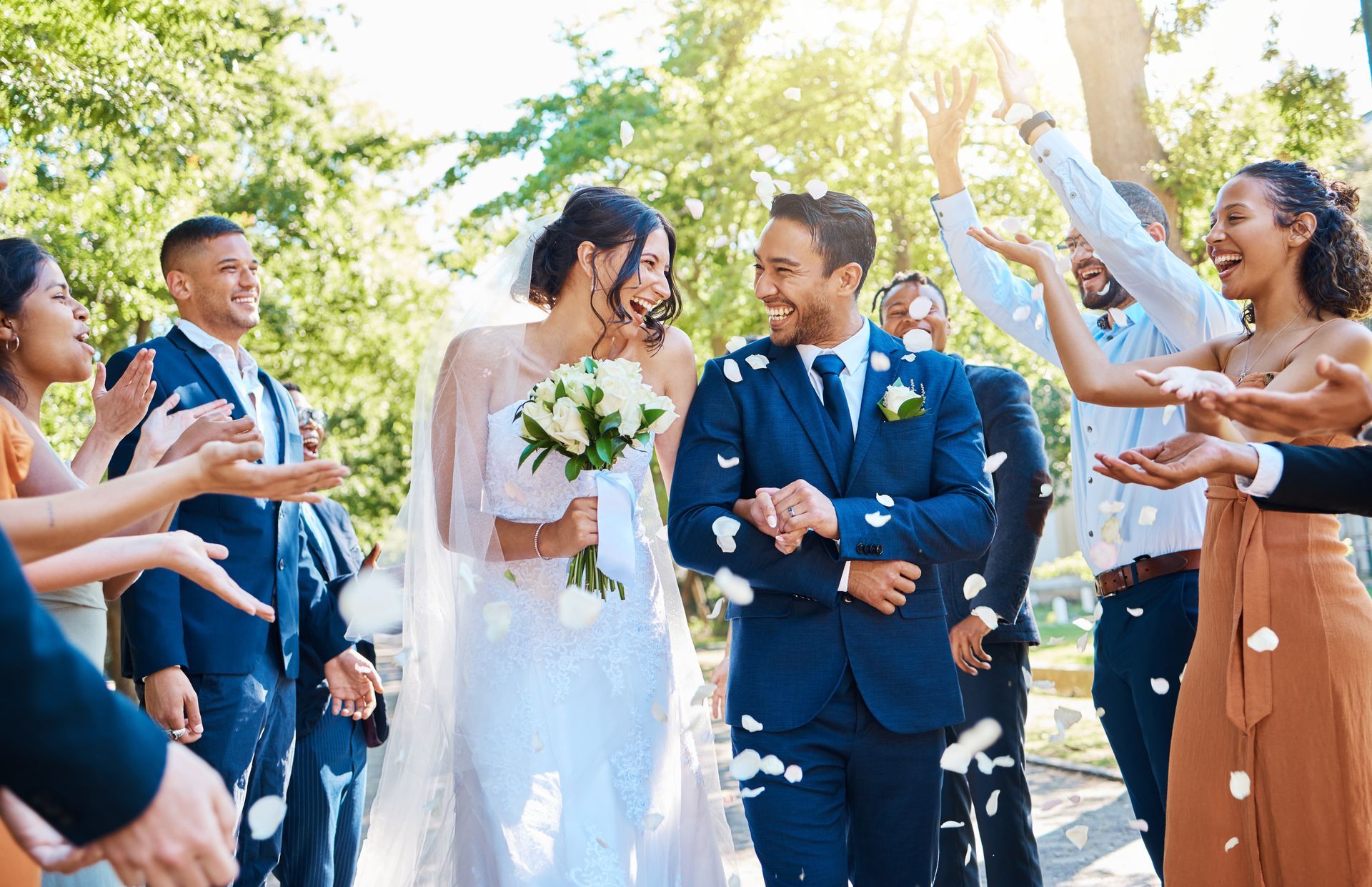Newlyweds walking through a cheering crowd of guests outdoors, smiling and throwing confetti