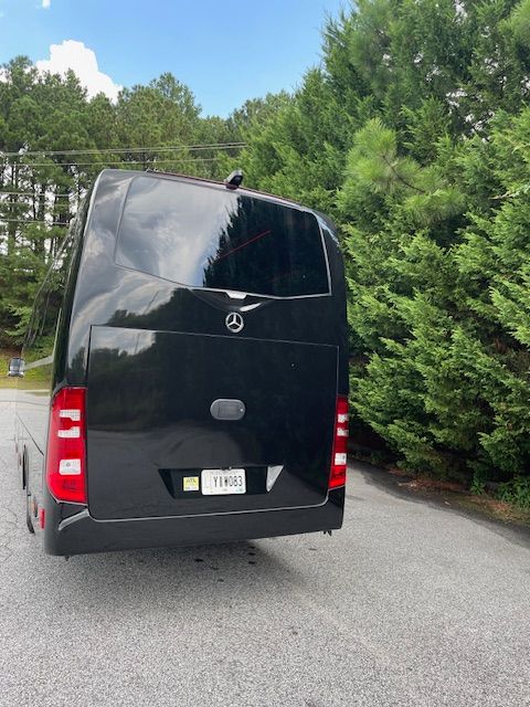 Black cargo van on a road beside green trees, viewed from the rear.