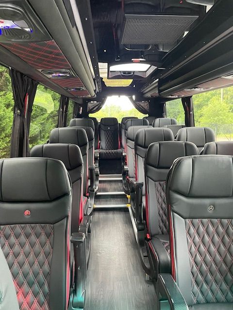 Interior of a luxury coach bus with rows of black and red quilted seats and an aisle view.