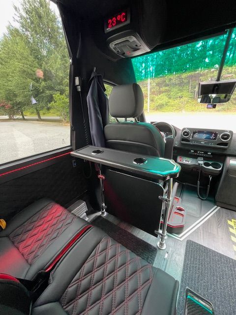 Luxury van interior with quilted black-and-red seats, foldout tray table, and dashboard view