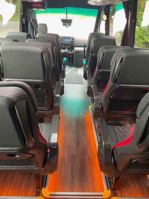 Interior of a shuttle bus with black seats and a wood-pattern aisle, viewed from the rear.