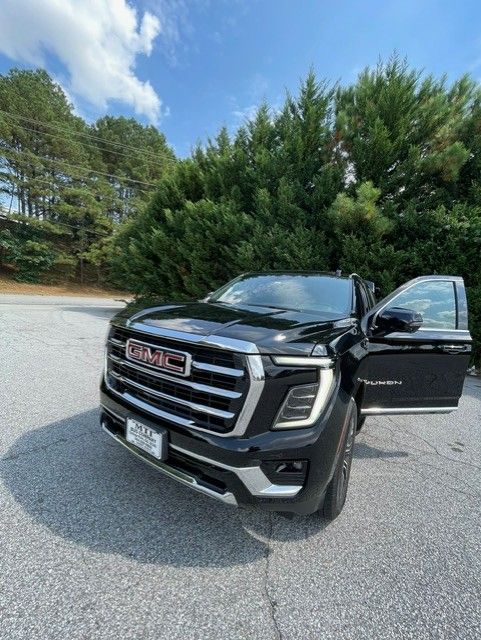 Black GMC pickup truck parked outdoors with the driver door open on a paved lot near trees