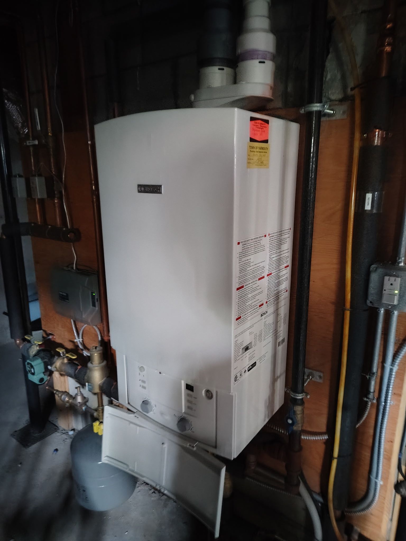 White wall-mounted boiler with exposed pipes and ventilation in a utility room setting.