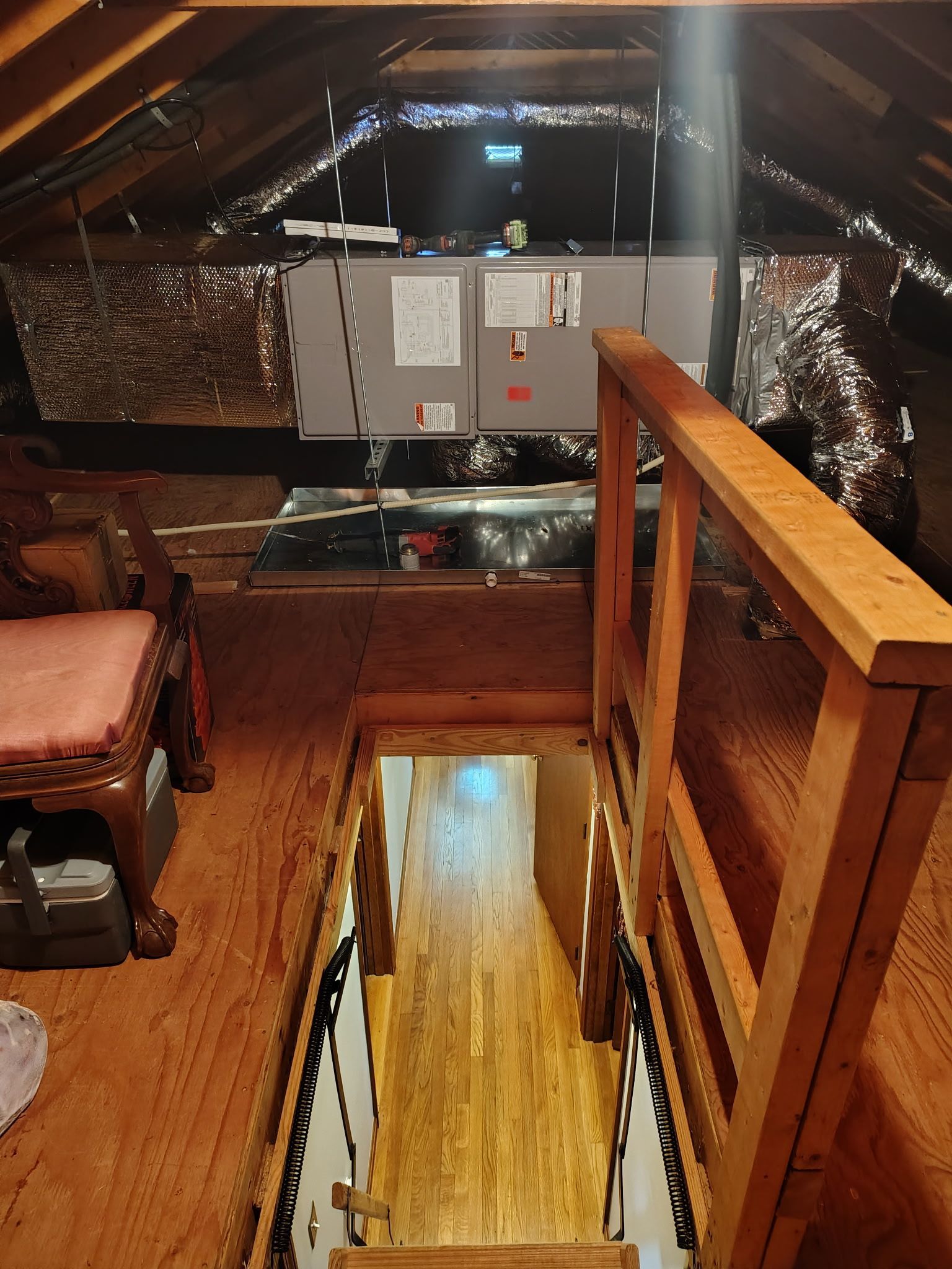 Attic with HVAC unit, stairs, and wooden railing.