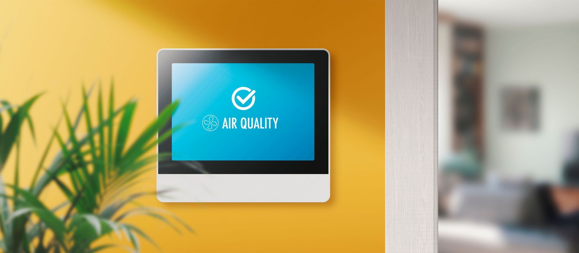 Air quality monitor on a yellow wall with text "Air Quality" displayed. A plant is in the left foreground.