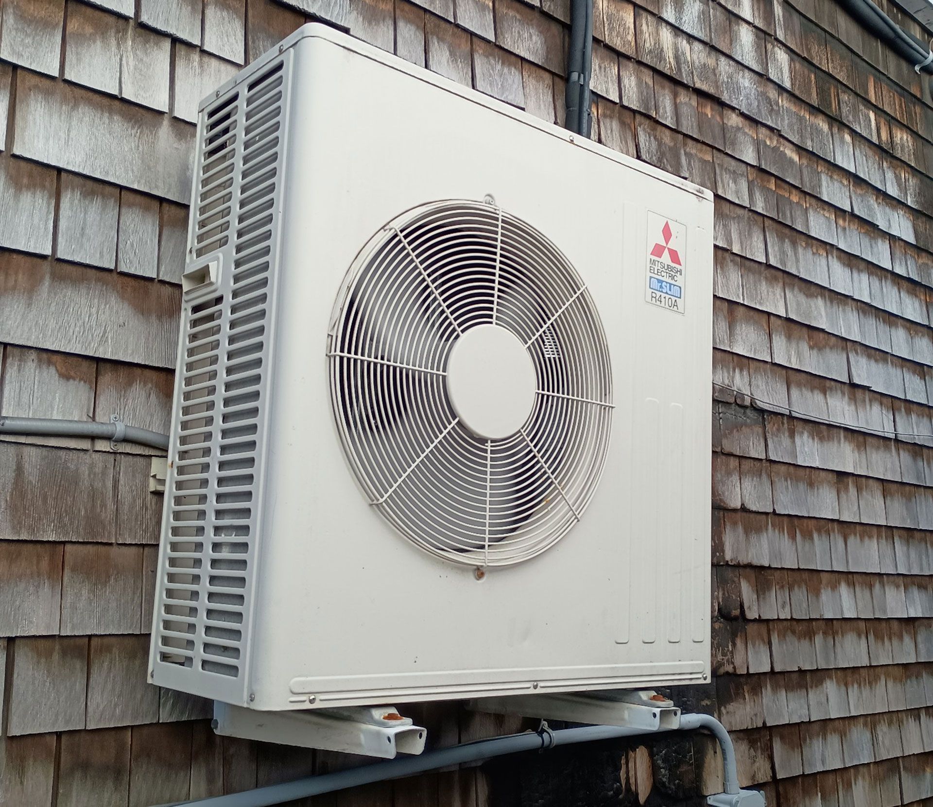 Mitsubishi heat pump unit mounted on a wood-shingled exterior wall.