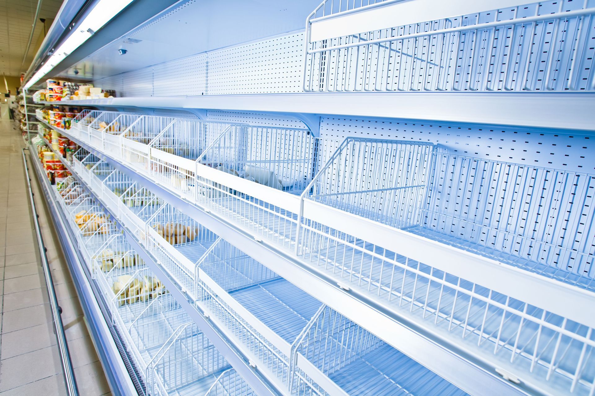 Empty grocery store shelves; focus on white wire baskets and shelving.