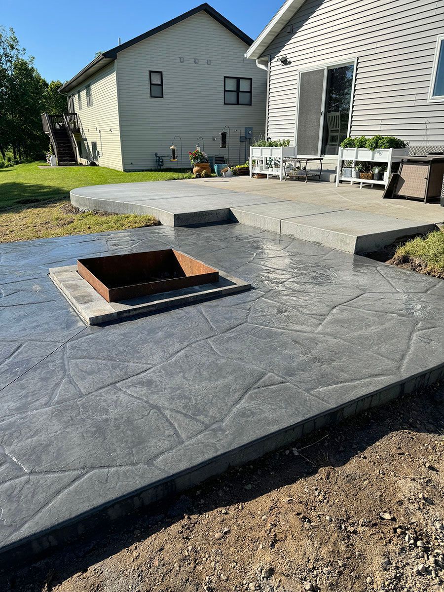 A patio with a fire pit in the middle of it and a house in the background