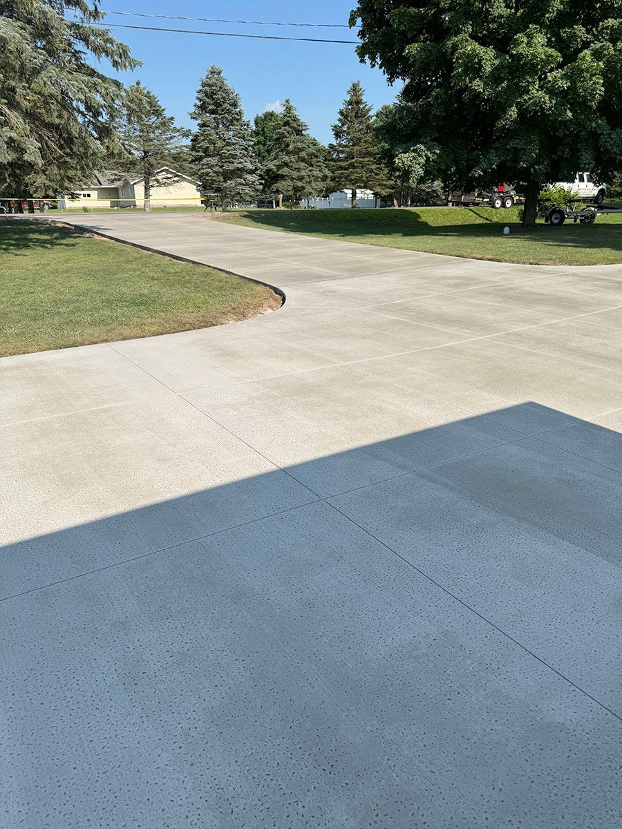 A concrete driveway leading to a house with trees in the background