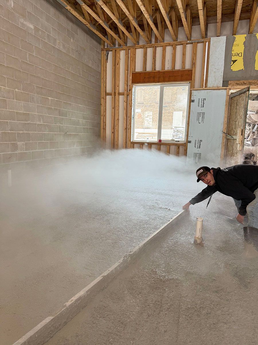 A man is laying a concrete floor in a room under construction