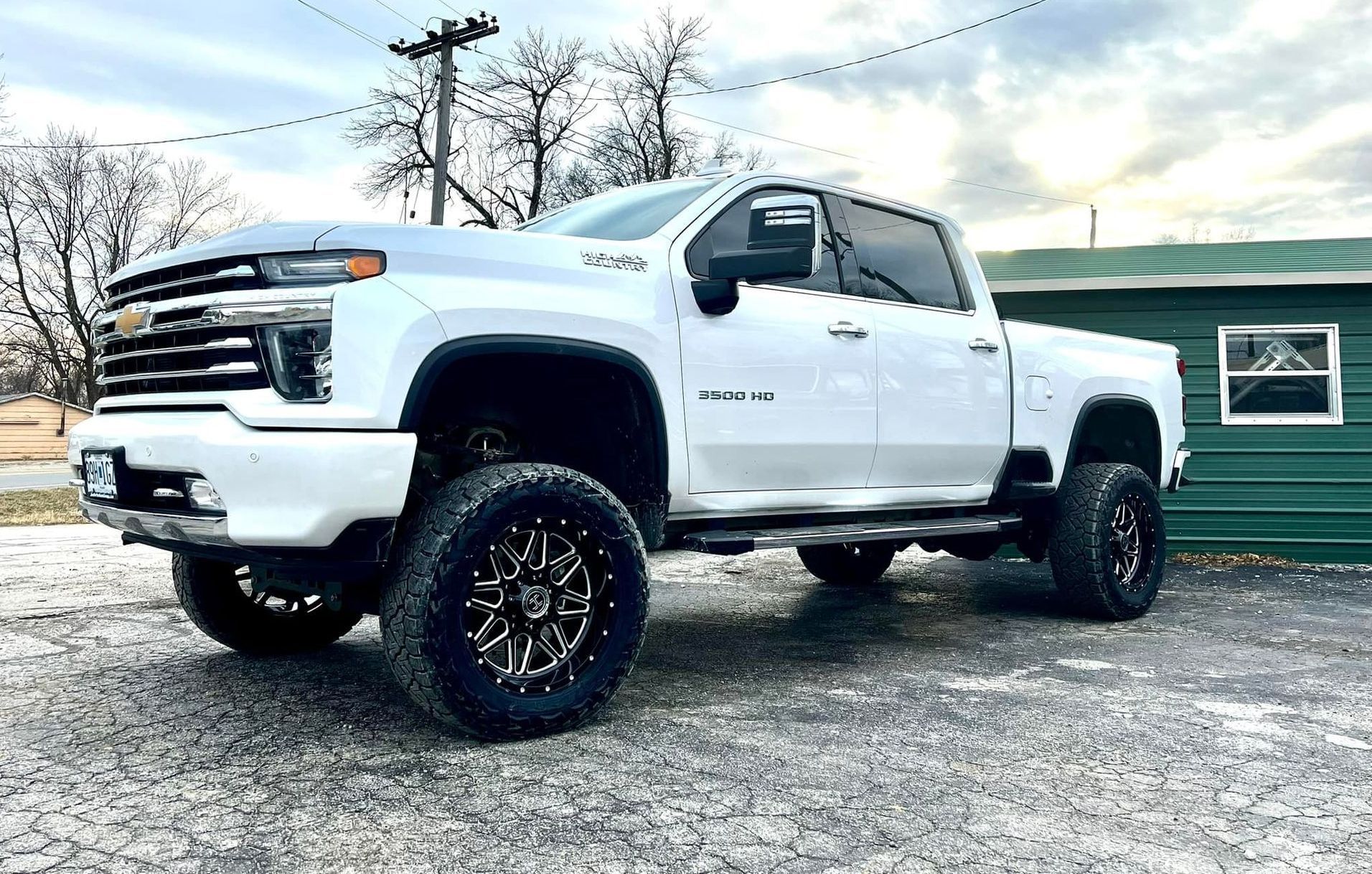 A white truck is parked in front of a green building.