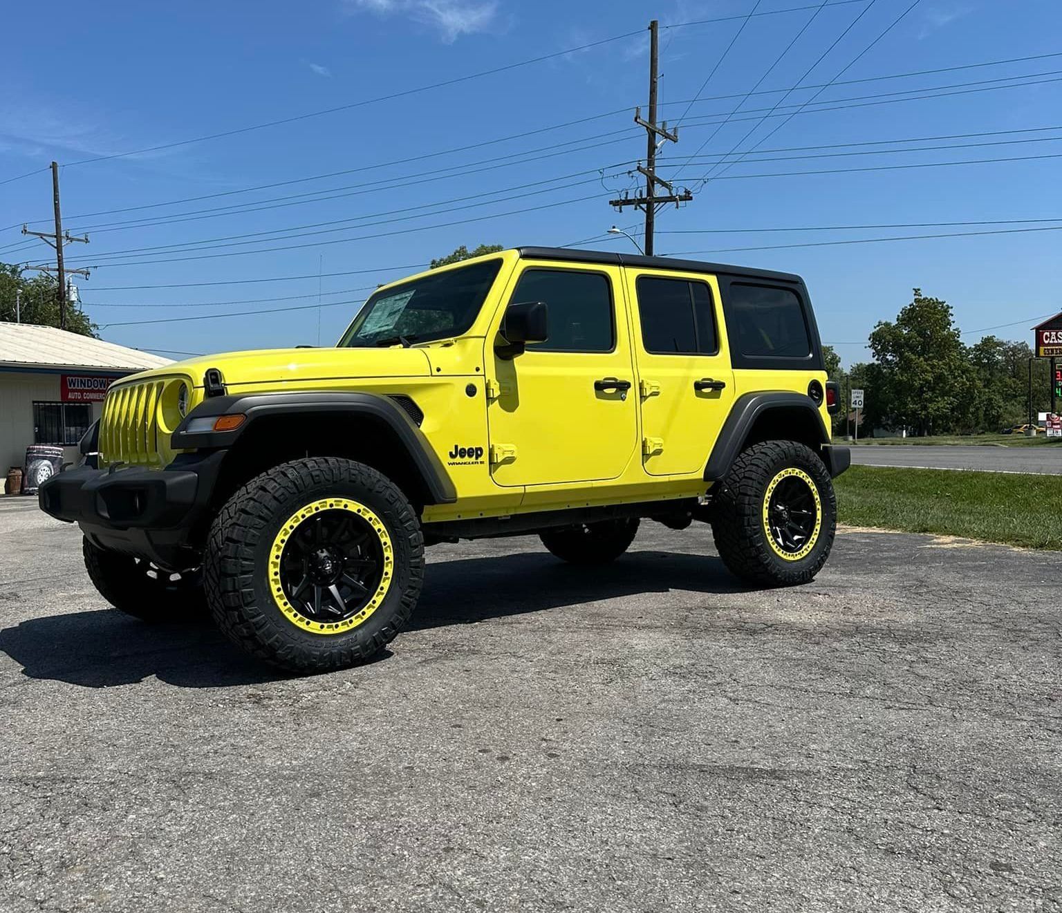 A yellow jeep wrangler is parked in a parking lot.