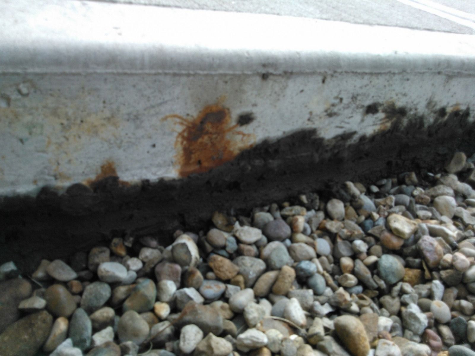 A close up of a concrete surface with rust on it surrounded by rocks.
