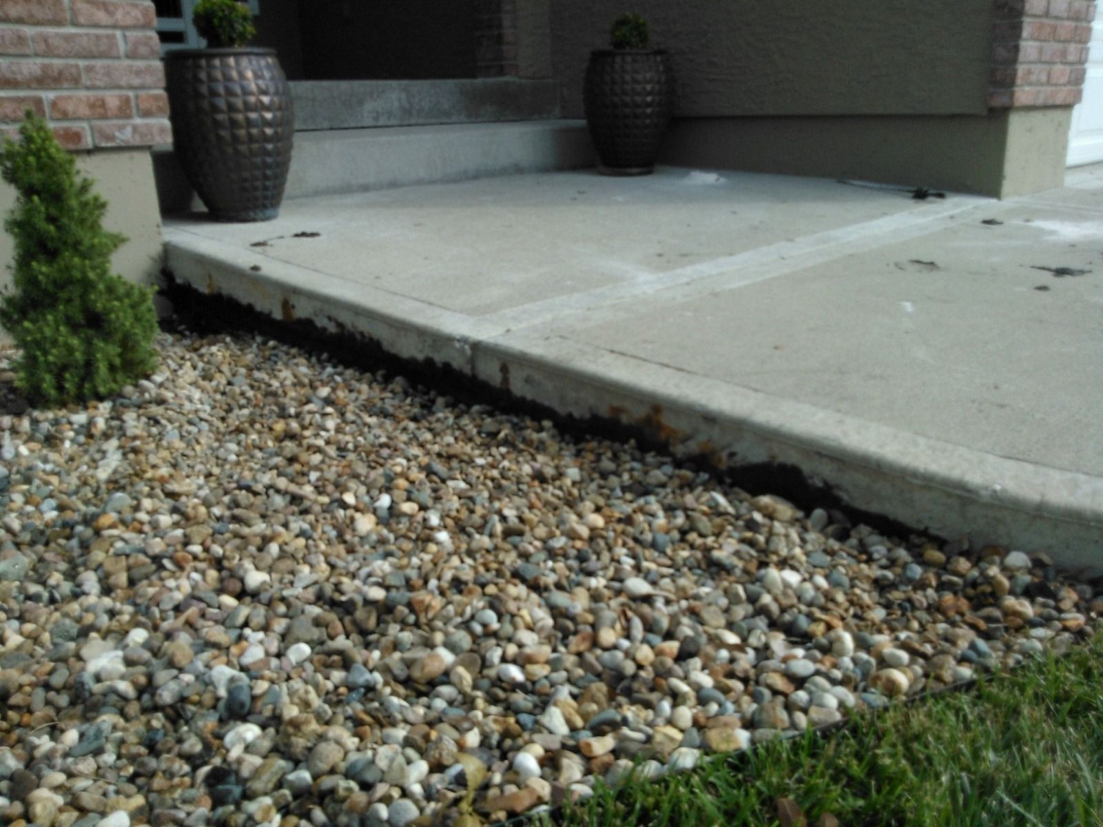 A concrete walkway with a gravel border in front of a brick house