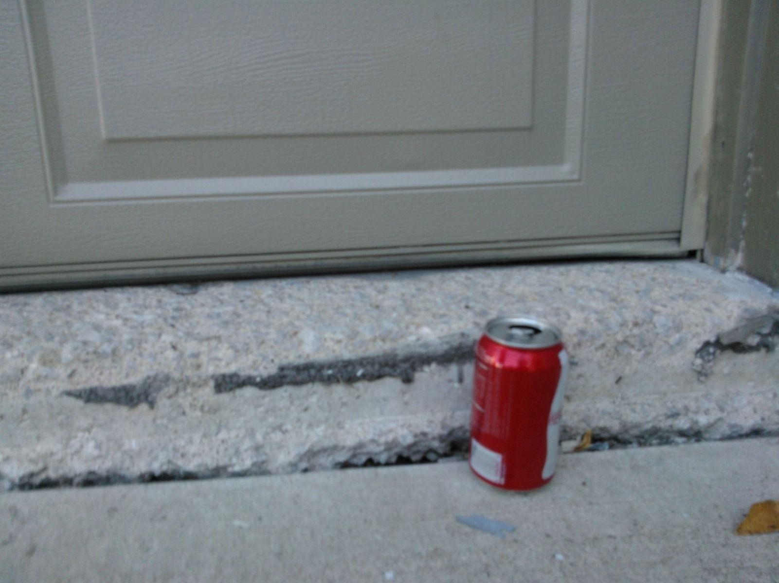 A can of soda is sitting on the sidewalk next to a door.