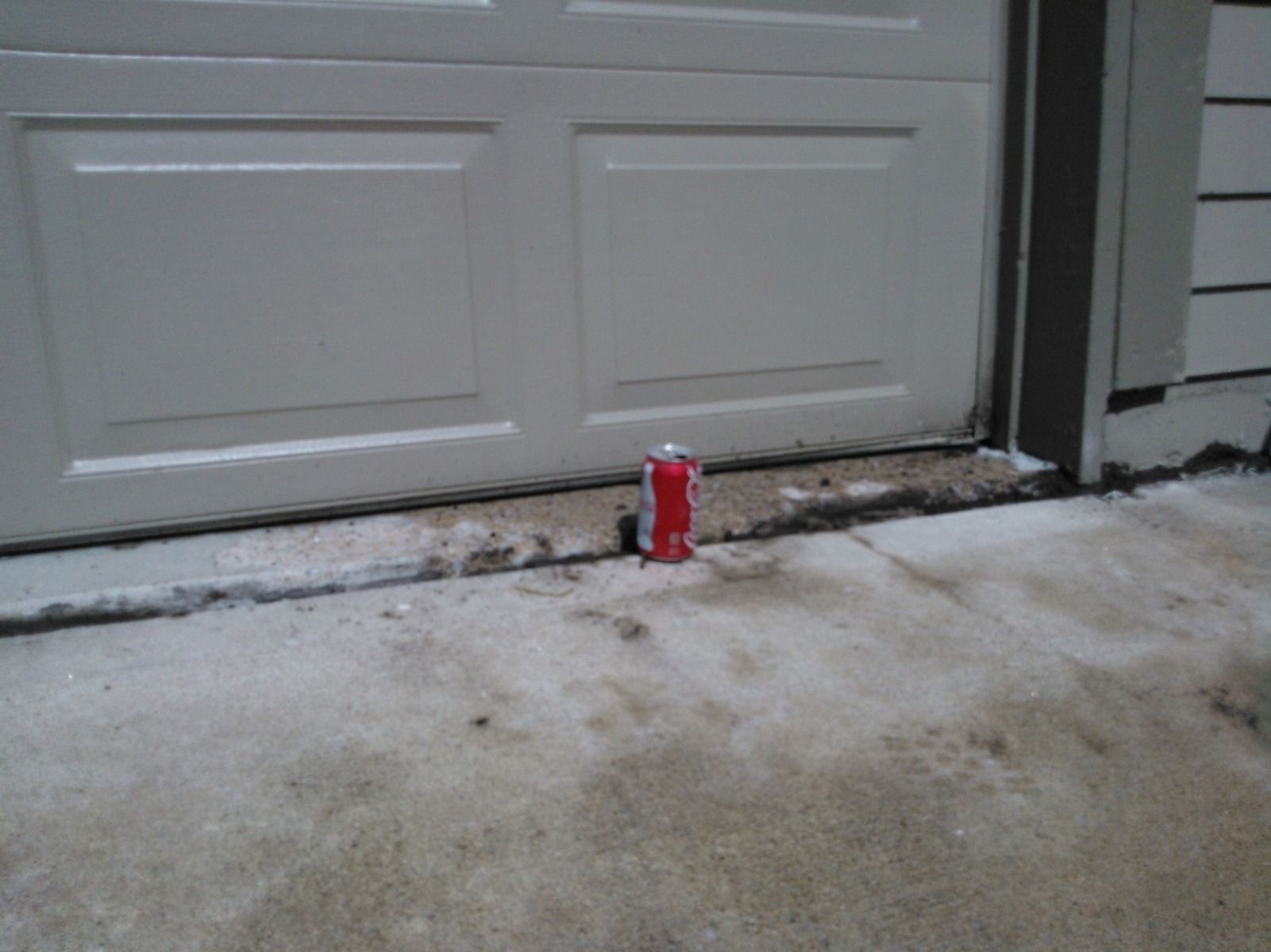 A can of coca cola is sitting on the ground in front of a garage door.