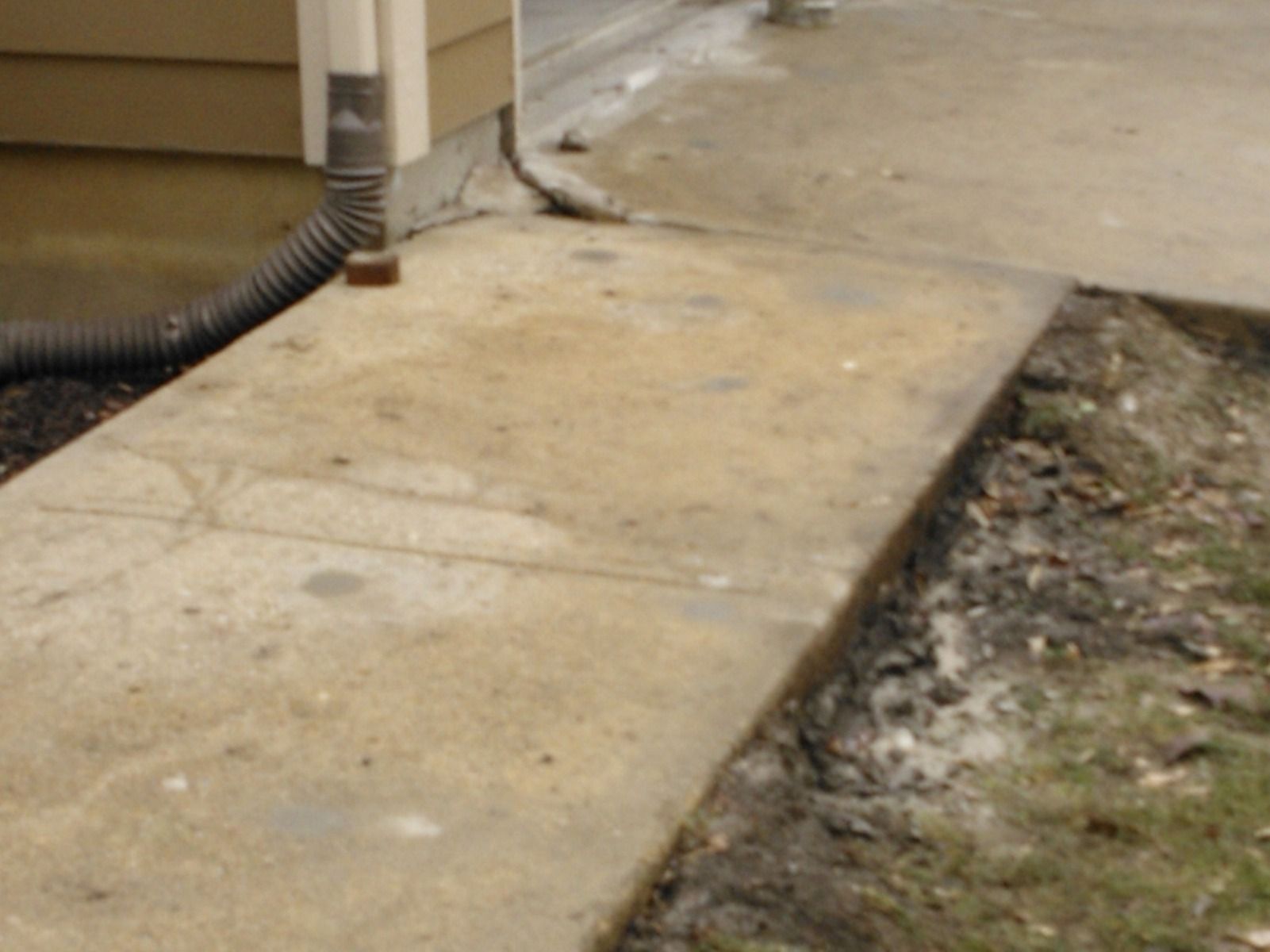 A drainpipe is attached to a sidewalk next to a house