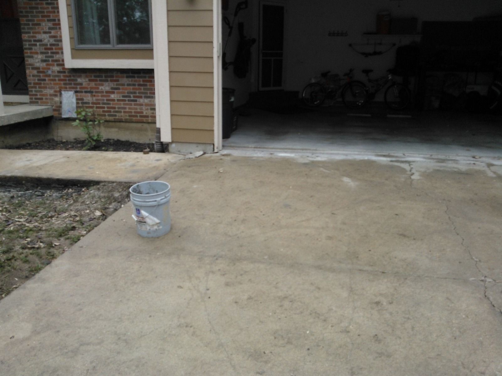 A bucket is sitting on the sidewalk in front of a garage