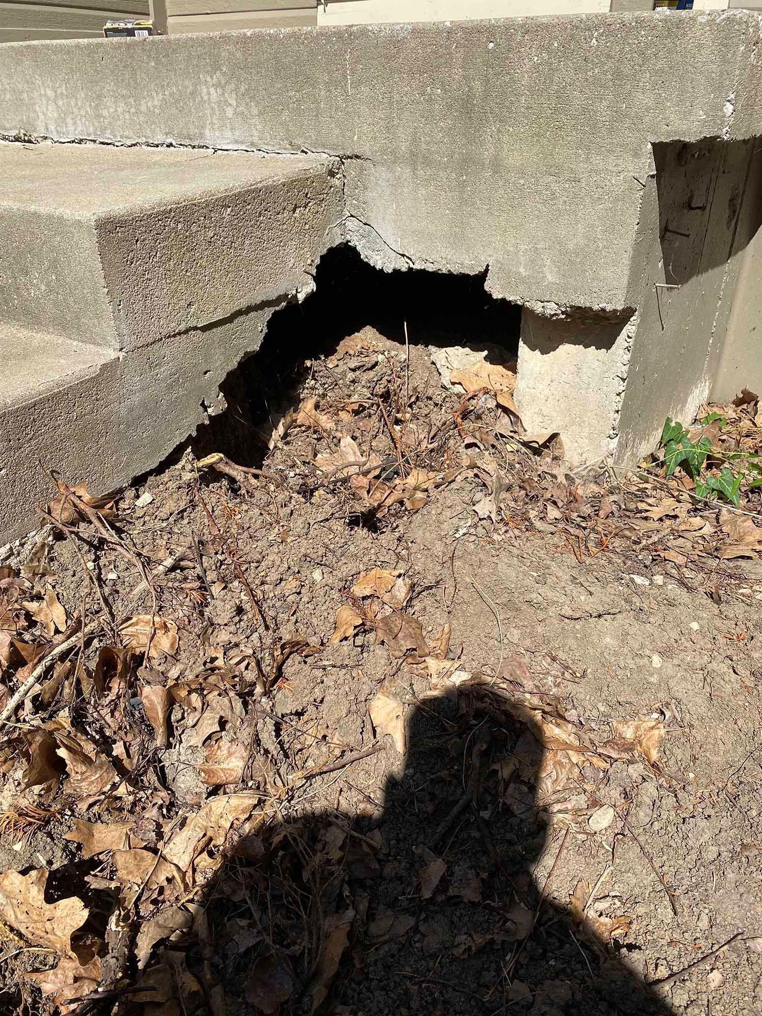 A shadow of a person is cast on the ground next to a concrete wall.