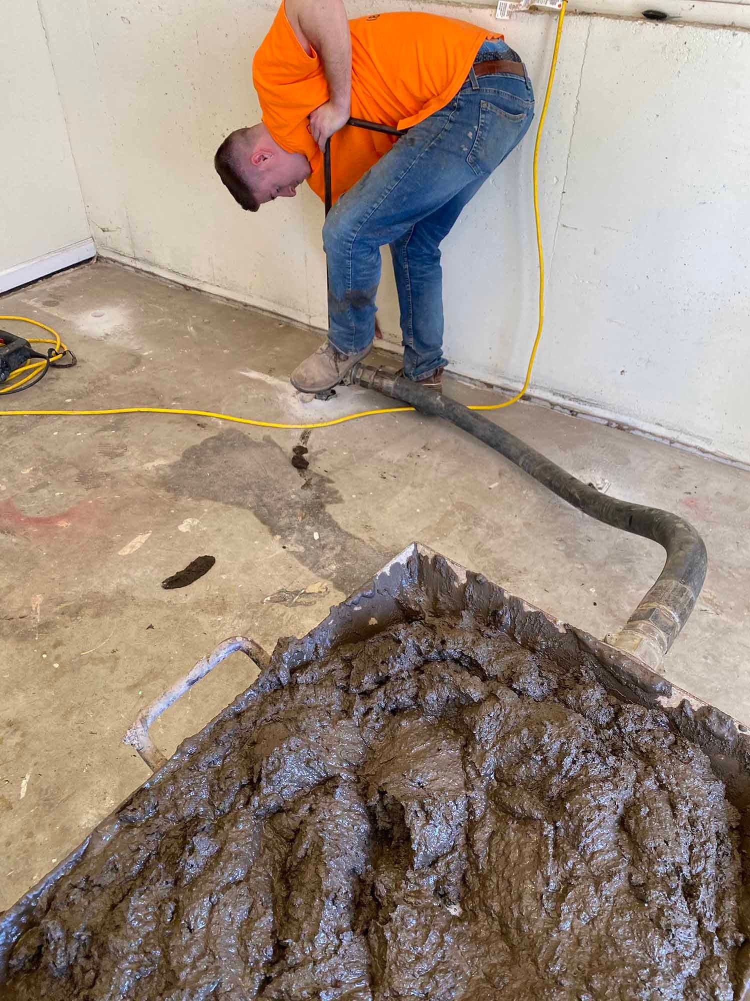 A man is bending over in a room with a vacuum hose.