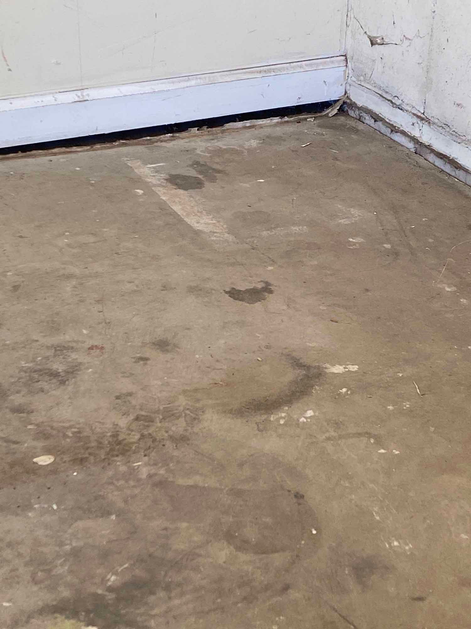 A dirty concrete floor in a room with a white wall.