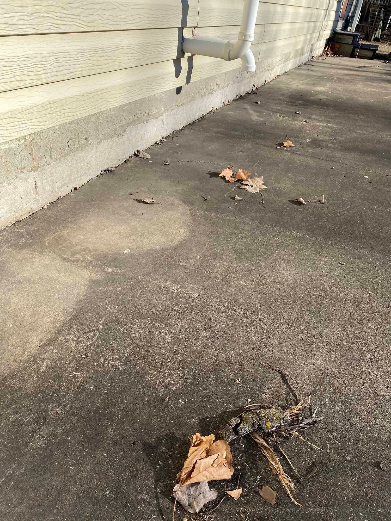 A drain pipe is sitting on the sidewalk next to a house.