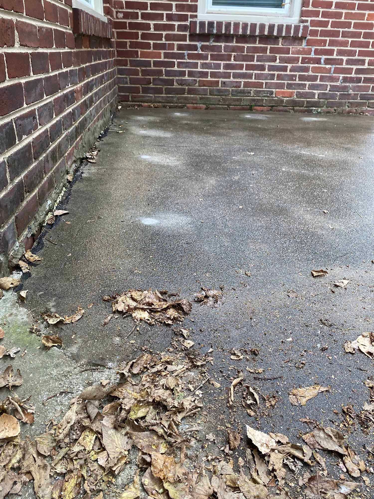 A concrete driveway with leaves on it next to a brick wall.