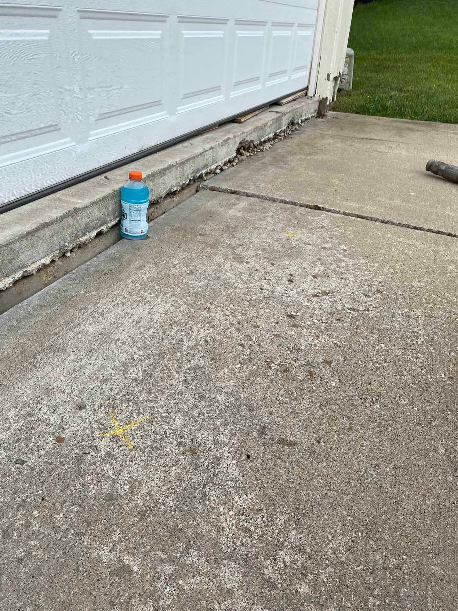 A bottle of clorox is sitting on the sidewalk next to a garage door.