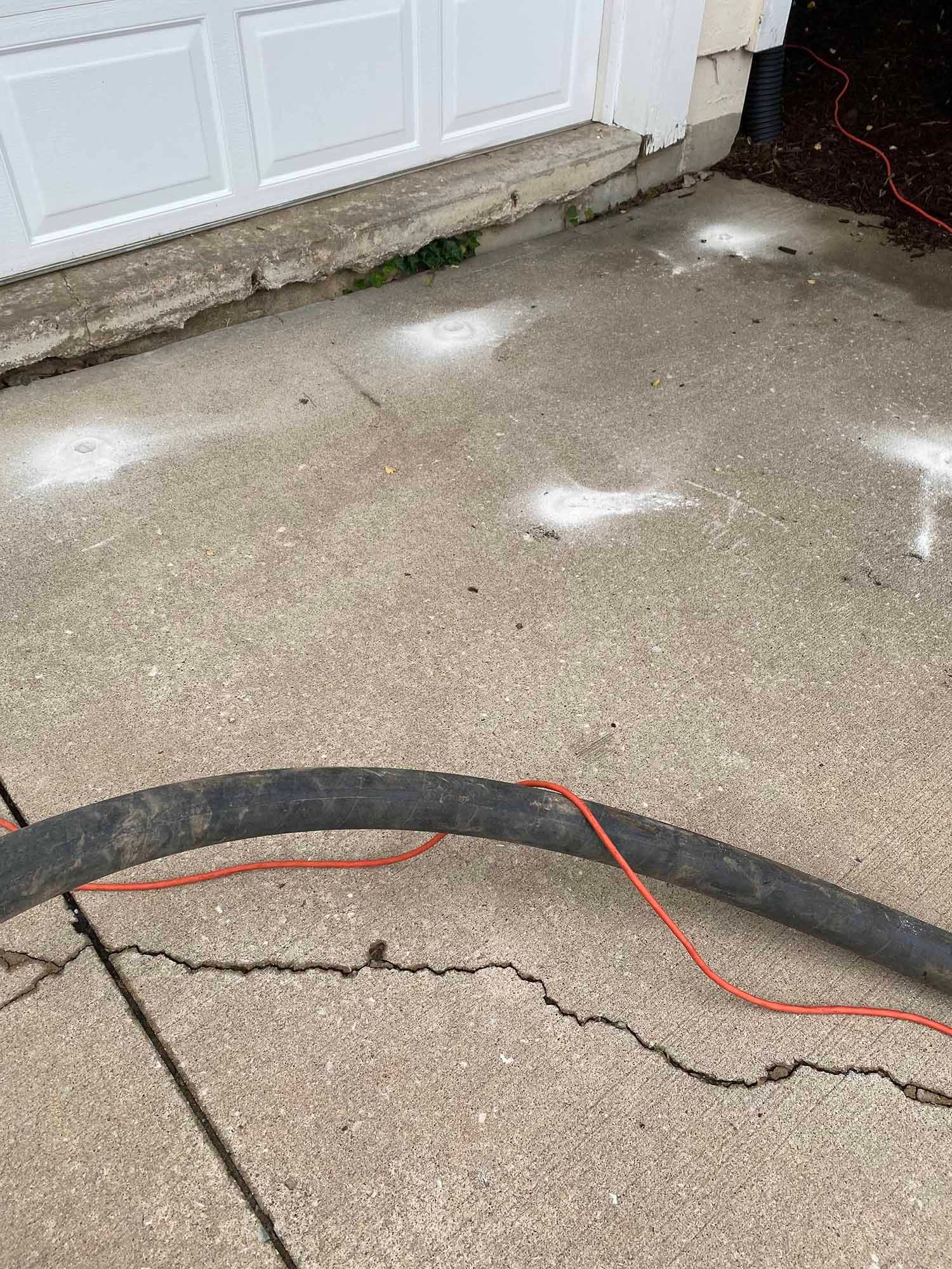 A hose is sitting on top of a concrete driveway next to a garage door.