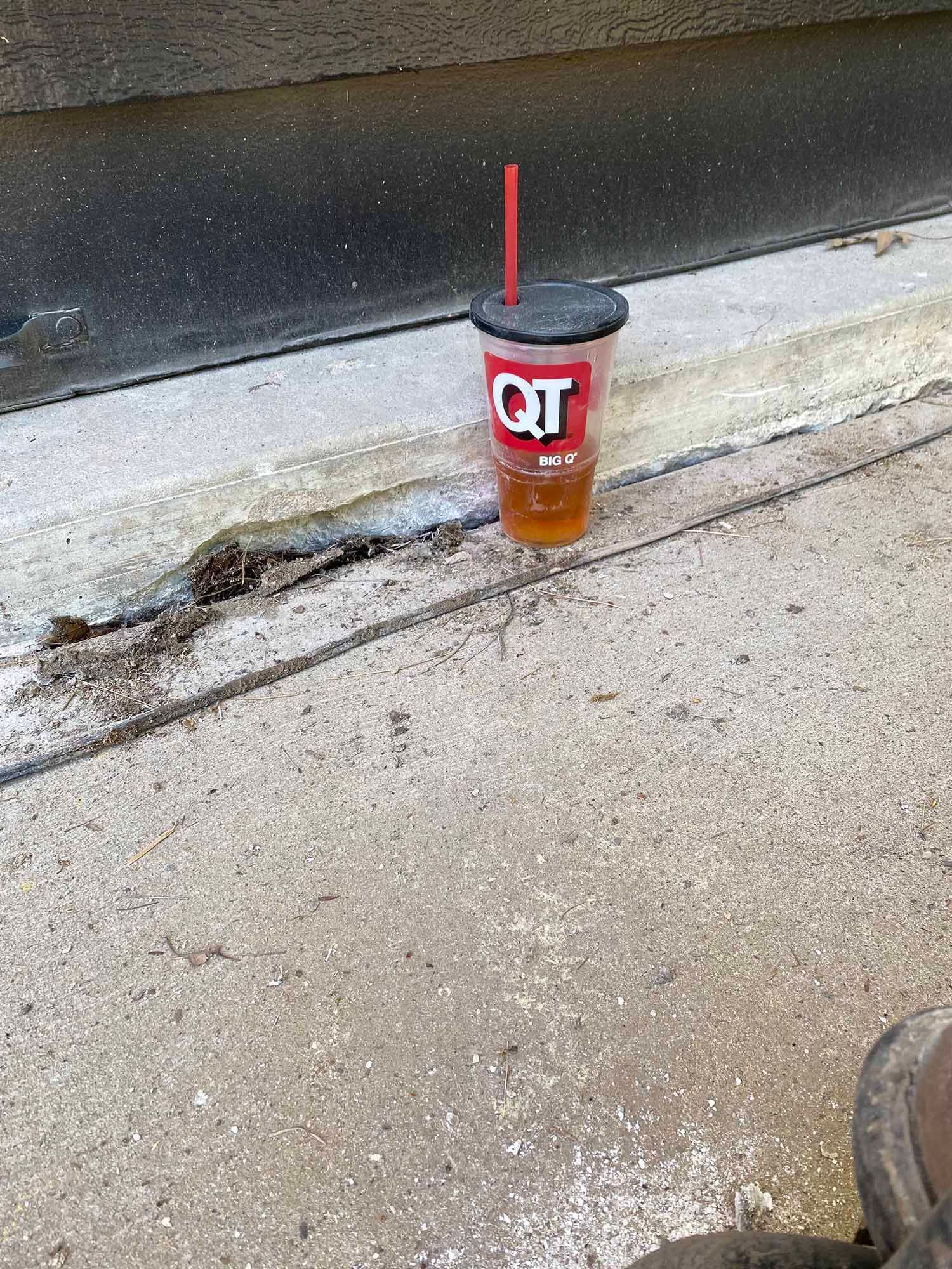 A cup of coffee with a straw is sitting on the sidewalk.