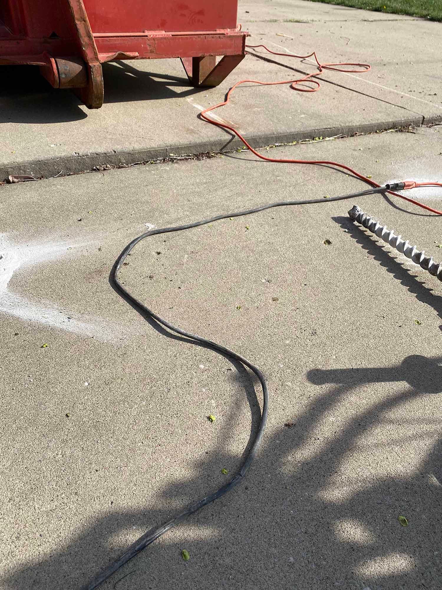 A hose is sitting on the sidewalk next to a red dumpster.