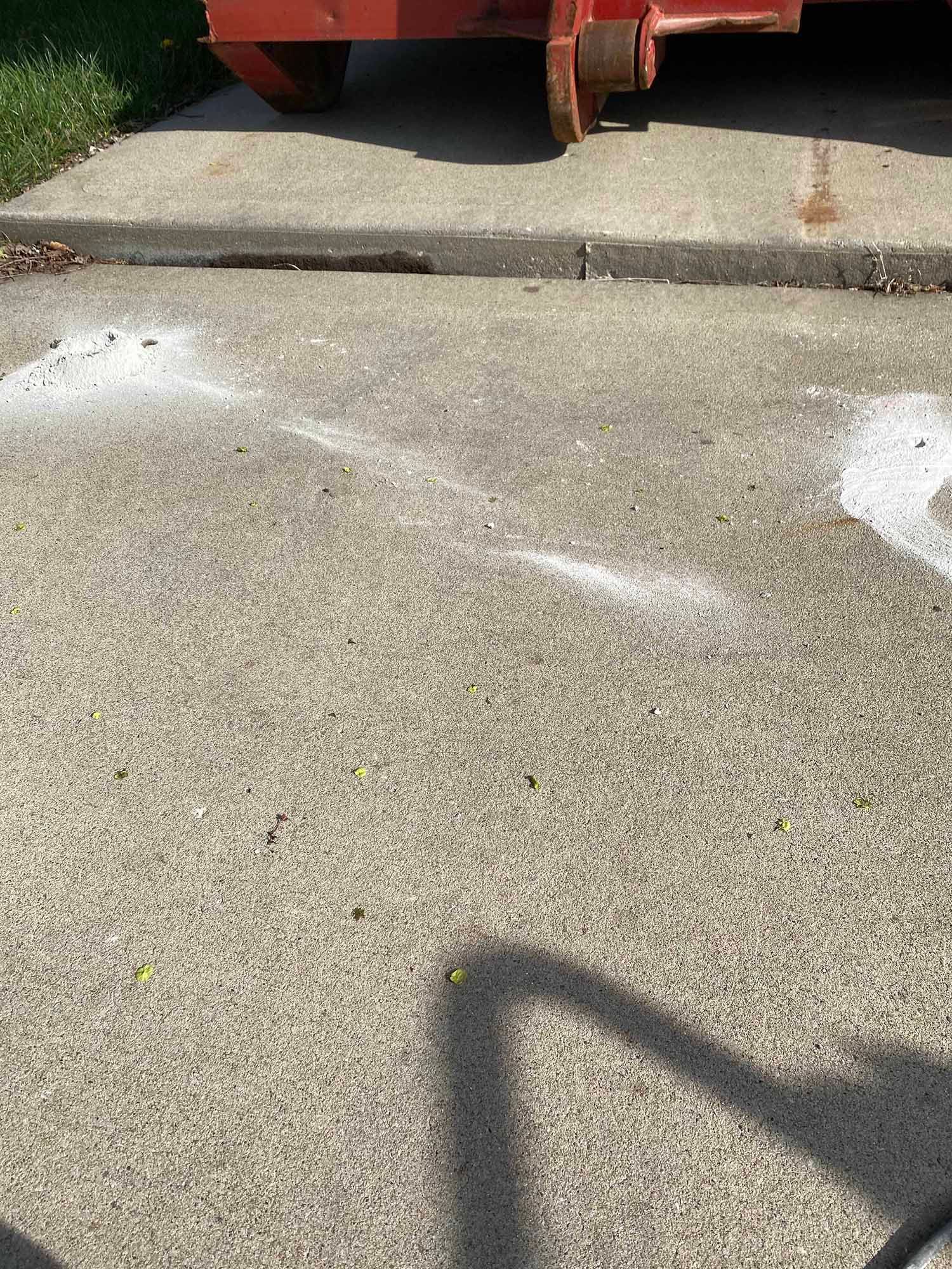 A red dumpster is parked on the side of a concrete driveway.