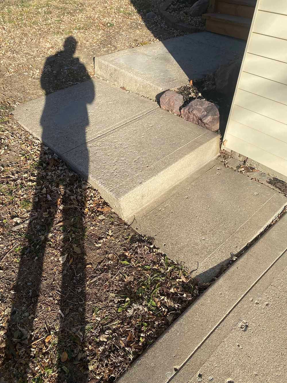 A person 's shadow is cast on a sidewalk next to a house.