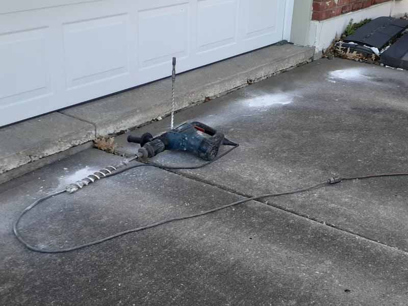A hammer drill is sitting on the ground next to a garage door.